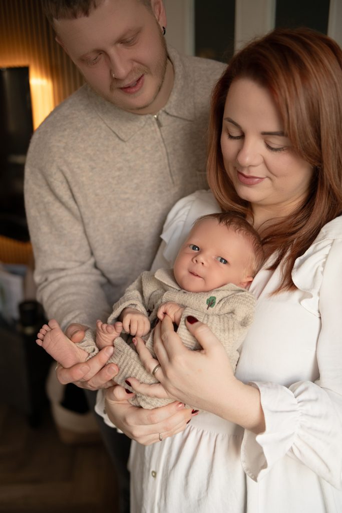 Home newborn photography in Ayrshire showing parents cuddling their newborn baby at home